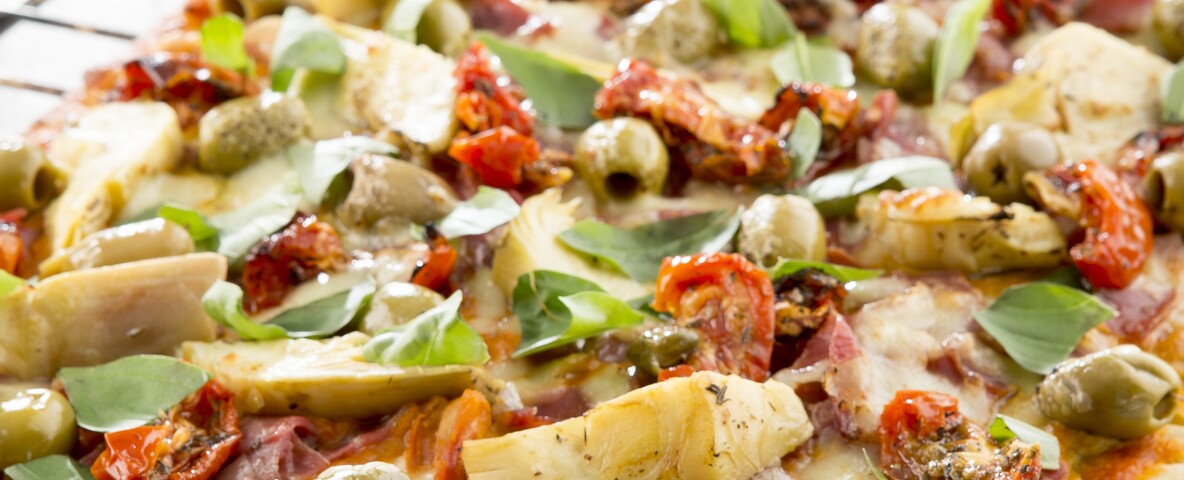 Pizza basilicum olijven ham artisjok zongedroogde tomaten